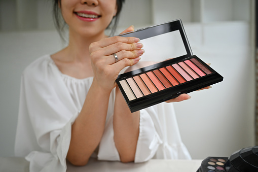 Smiling young woman holding a makeup palette while recording video for her channel. Influencer, blogger and lifestyle concept.