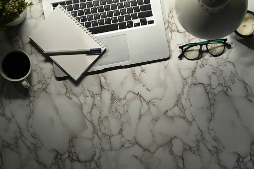 Laptop, notepad, coffee cup and glasses on marble. Top view with copy space for text.