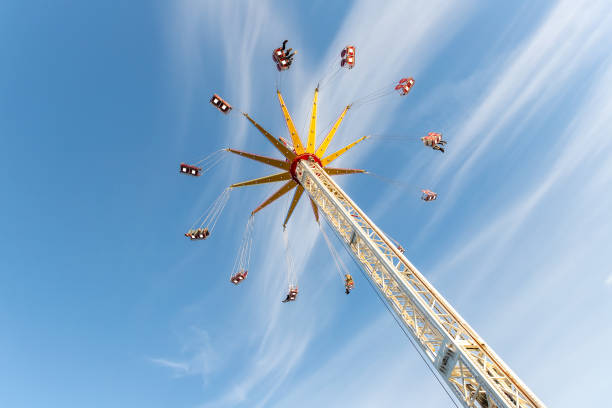 Scenic bottom view high chain swing flying carousel against blue sky. Merry go round roundabout chairoplane at portable amusement park. People enjoy having family fun play riding at fair festival.