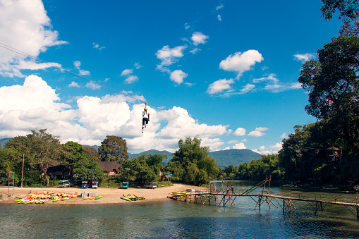 Adventure-loving tourists are ziplining across the Song River. during the clear sky in Vang Vieng, Laos