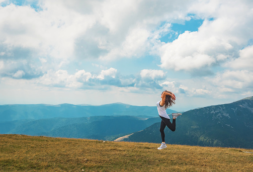 A young woman jumps up for joy in a beautiful mountain landscape.