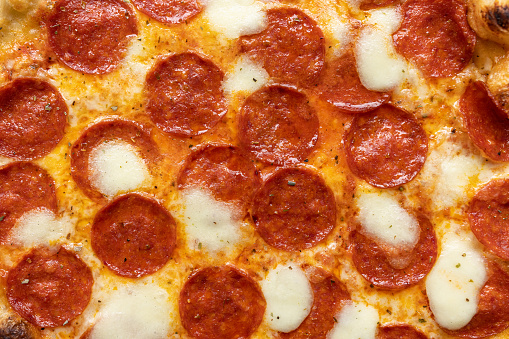 Extreme close-up of pizza with pepperoni and cheese isolated on a blue background
