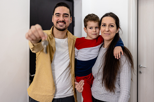 A woman and a man with a little kid are entering a new apartment with happiness and enjoyment.