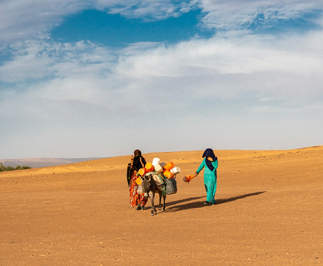 Sahara Desert, Morocco - May 12, 2023:  Berber women with a donkey going for water. Sahara desert, Morocco, Africa.