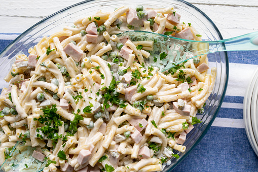Traditional german pasta salad, homemade cooked with macaroni noodles, green peas, pickles, sausage and mayonnaise. Served ready to eat in bowl with cutlery. Closeup, Top view