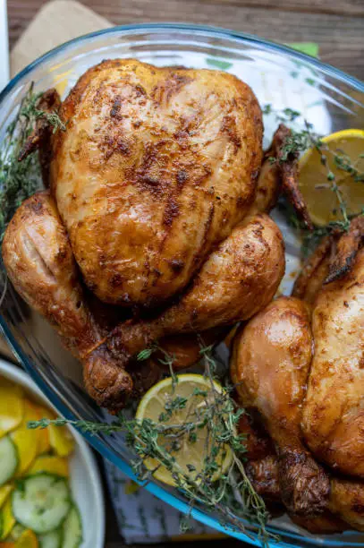 Homemade oven roast chicken with lemon and thyme. Served hot and ready to eat in a baking dish on wooden table. Closeup, top view