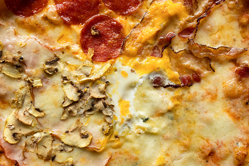 Extreme close-up picture of pizza with different ingredients separated into four  sections, isolated on a blue background