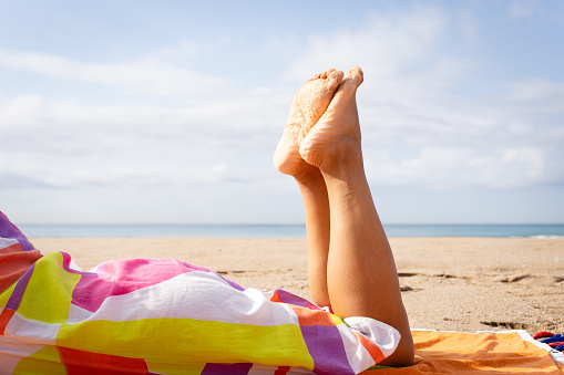 Closeup of woman legs lying on the beach with bare feet enjoying a day at the beach in summer on the sand and wearing a colorful eye catching dress