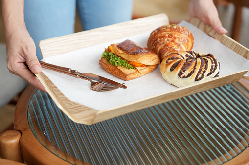 Cropped shot of a woman holding a serving tray with assortment of pastries and bread buns