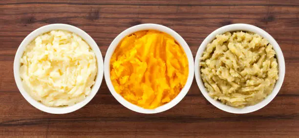 Top view of three bowls containing variety of purees (potato, squash, sweet potato)