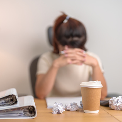 Coffee disposable cup against woman having Tired and Stressed while working, female businesswoman having headache and Migraine at office or Home late night. Overworked and Overtime