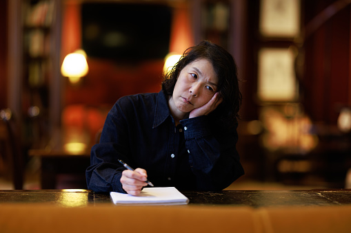 Asian woman sitting at her old leather bound desk about to write in a notepad.