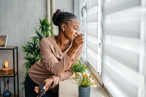 Portrait of a beautiful young black woman looking out the window of her apartment.