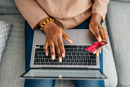 Beautiful young black woman shopping online at home, using credit card and a laptop.