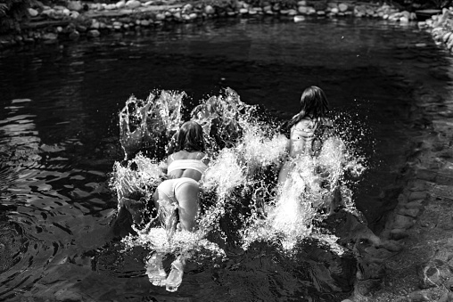 Two little girls jump in swimsuits into a lake with cold water on a hot summer day