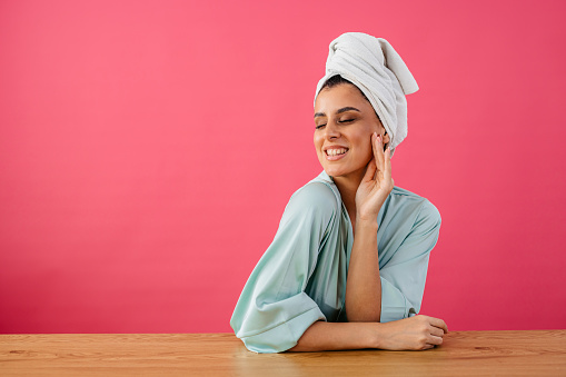 Portrait of a beautiful young woman in a bathrobe standing against a pink background.