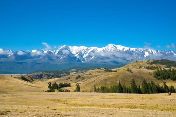 istock Scenic view from sunlight grassy hill with road to high mountain range. Beautiful sunny mountain landscape with large snow peak mountains. Road trip to Altai. 1648192037