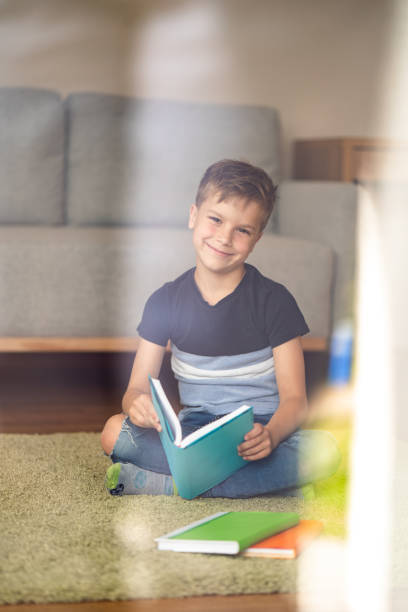 istock Cute boy holding a book at home and looking at camera 1648192130