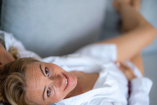 Happy woman lying on the sofa wearing white shirt and looking at camera