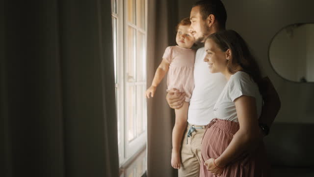 SLO MO Loving Pregnant Couple With Daughter Looking Through Window at Home