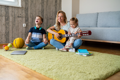 Happy woman playing guitar whit her son and daughter at home