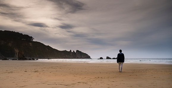 Figure of a mature woman walking along a lonely beach at sunset with her back to the camera.