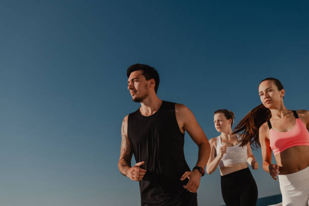 Three confident young people in sportswear looking concentrated while jogging outdoors together