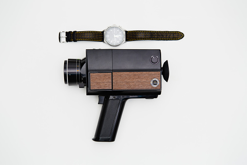 Old fashioned analog Super8, 8mm film movie camera and a wristwatch on white background. Deadline for movie making