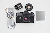 Vintage SLR camera, lenses and lightmeter set with some blank polaroid-like frames and dia slides on white background