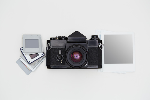 Film SLR camera and some dia slides with blank polaroid-like photographs on white background