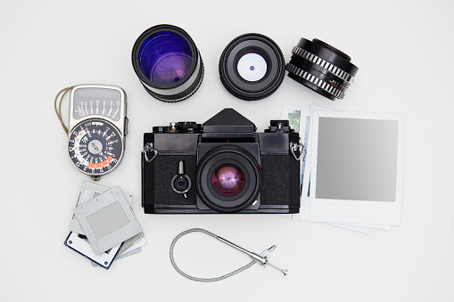 Vintage SLR camera, lenses and lightmeter set with some blank polaroid-like frames and dia slides on white background