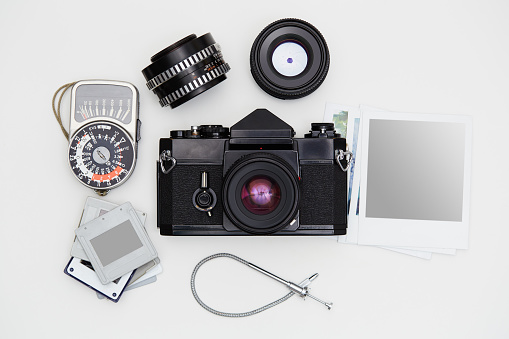 Vintage SLR camera, lenses and lightmeter set with some blank polaroid-like frames and dia slides on white background