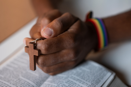 Man wearing LGBT rainbow bracelet with Holy Bible