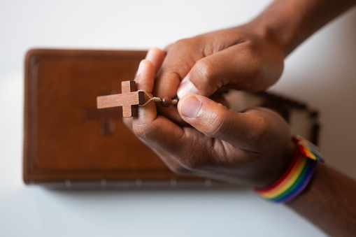 Man wearing LGBT rainbow bracelet with Holy Bible