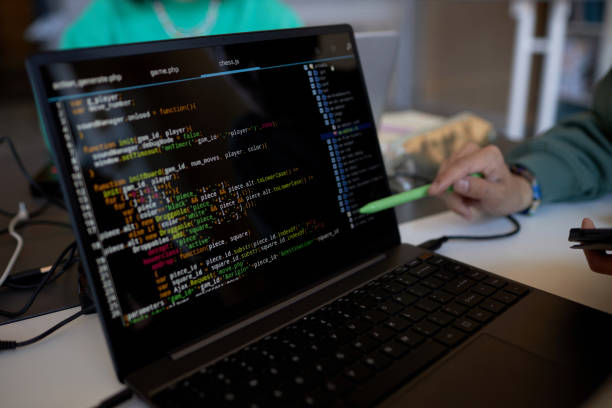 istock Focus on laptop screen with coded data and pen held by hand of young man 1648248422