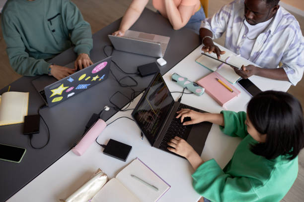 istock Above angle of team of young students sitting by table and using mobile gadgets 1648276681