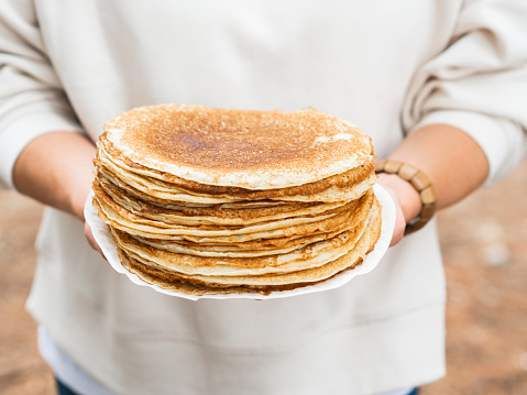 Women holding white plate with pile thin pancakes. Many pancakes are stacked. Thin pancakes with crispy crust. Pancakes for breakfast and carnival. Food background.