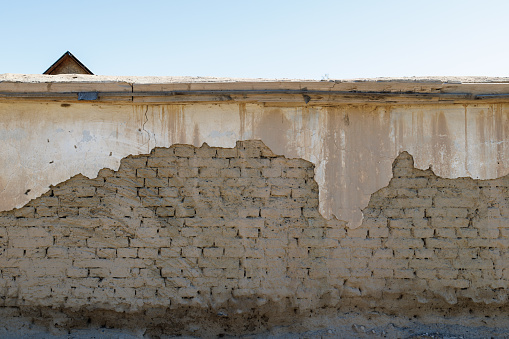 old adobe building wall with peeled off dirty white plaster layer leftovers