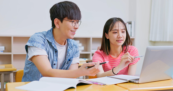 asian college students with laptop computer are sitting in a classroom and discussing happily at university