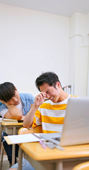 asian college students with laptop computer are sitting in a classroom and discussing with negative emotion at university