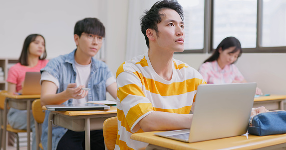 asian college students with laptop computer are sitting in a classroom and paying attention during class at university