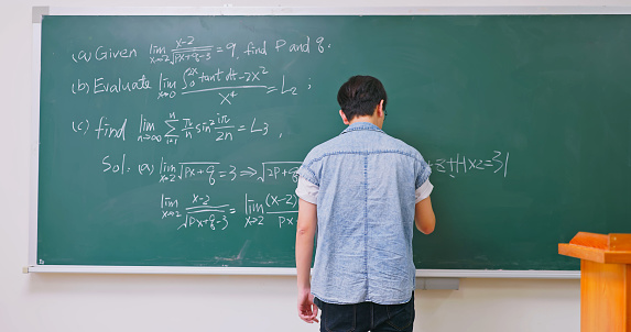 rear view asian male teacher or college student is writing on blackboard during class in classroom at university