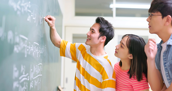 asian college students are writing on blackboard and discussing formula in classroom at university