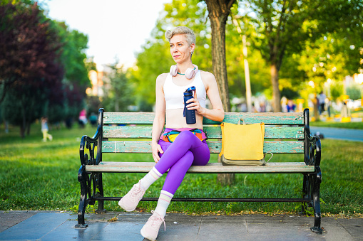 fit athletic short hair woman sitting on bench in park and drinking water