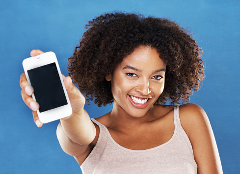 A pretty young woman showing you her smartphone while isolated on a blue background