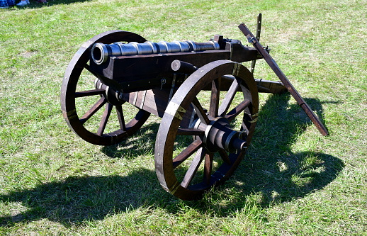 A close up on a metal cannon set inside a wooden frame and attached to some wheels for more mobility seen in the middle of a field, meadow, or pastureland during a historical fair organized in Poland
