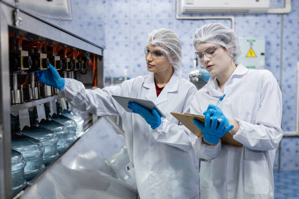 istock Female worker using tablet checking quality  drinking water before process of filling water into plastic bottles to bring out to consumers. Water bottles on production line of factory. 1648349248