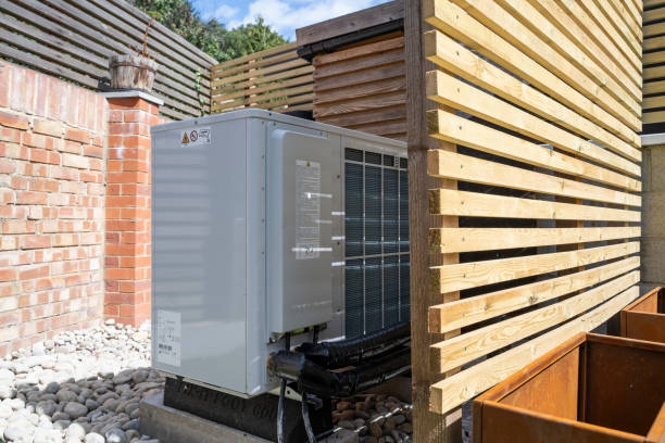 Rear view of the air source heat pump outside in the garden, between a wooden fence and brick wall on a sunny day.