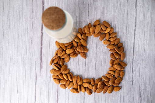 Almond milk in a bottle surrounded by heart shaped almonds.