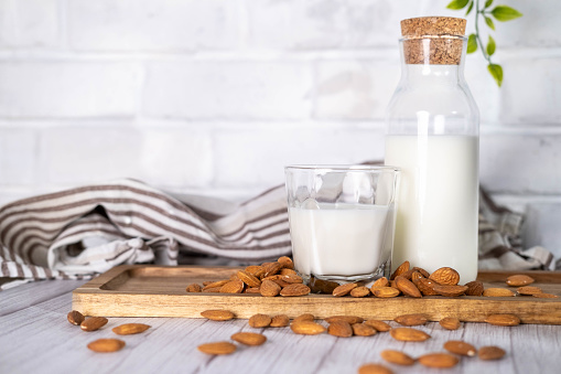 Almond milk in glass bottle and almonds on the kitchen table.